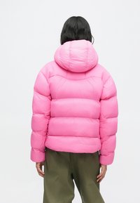 Chaqueta de plumón rosa con capucha, que presenta un diseño acolchado, textura suave y puños elásticos, combinada con pantalones verde oliva.