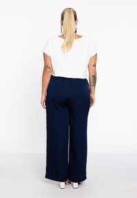 Witte top met korte mouwen gecombineerd met marineblauwe wijde broek. De outfit heeft een relaxed fit en een soepele stoftextuur.