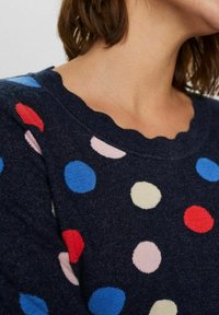 Mornarsko modra pulover s valovitim ovratnikom, okrašen z večbarvnimi pikami v rdeči, roza, modri in krem barvi na mehkem, strukturiranem materialu.