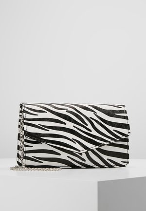 Zwart-witte clutchtas met zebraprint en een zilveren kettingriem, liggend op een witte ondergrond tegen een grijze achtergrond.