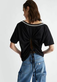 Top nero a maniche corte con scollatura a barca, retro arricciato e dettaglio con cordino regolabile. Tessuto morbido; vestibilità rilassata.