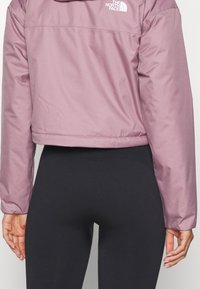 Kort, lätt jacka i mjukt lavendelfärgat tyg med en slät textur. Har en logotyp på övre delen av ryggen och elastiska manschetter.