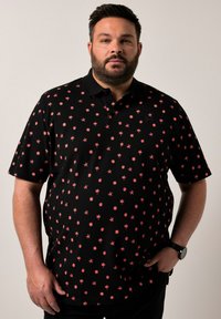 Černé polo tričko s potiskem mal ých červených hvězd a teček. Krátké rukávy, límeček a kapsa. Hladká textura, standardní střih.