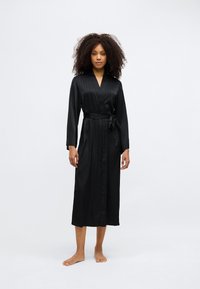 Μαύρη σατέν ρόμπα με μακριά μανίκια, λαιμόκοψη σε σχήμα V, κλείσιμο με ζώνη στη μέση και κατακόρυφες ρίγες κατά μήκος της. Μήκος μέχρι τη μέση της γάμπας.