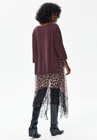 Sweter Pleh w głębokim burgundowym kolorze z rękawami 3/4, noszony na przezroczystej sukience w cętki z czarną koronkową lamówką, do tego czarne kozaki sięgające do kolan.