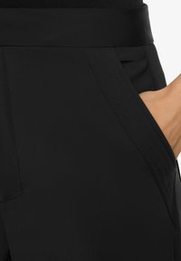 Black, smooth fabric pants with a wide waistband, featuring a side pocket and subtle stitching details, highlighting a tailored design.