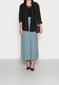 Zwarte blouse over een zwarte kanten top, gecombineerd met een vloeiende, lichtblauwe maxi-jurk en zwarte puntige hakken. Kleine zwarte handtas.