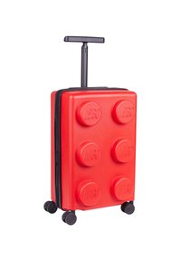 Red LEGO-themed suitcase with circular bumps, black zipper, retractable handle, and four wheels for mobility. Textured surface.