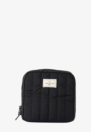 Trousse rectangulaire matelassée noire avec fermeture éclair et une étiquette rectangulaire blanche au centre à l'avant portant l'inscription "THE FLAT LAY CO. LONDON".