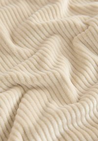 Soft beige textured fabric with wavy ribbed patterns, showcasing a plush, cozy surface ideal for blankets or upholstery.