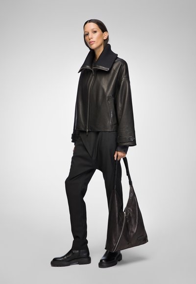 Black leather jacket with a high collar, paired with black loose trousers and ankle boots. Holding a large, dark, slouchy handbag.