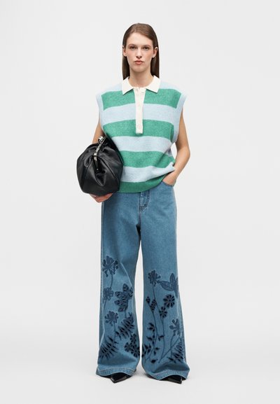 Pull en maille rayé vert et bleu clair, associé à un jean large en denim orné de broderies florales bleu marine. Sac noir pour compléter la tenue.