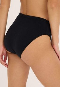 Culotte haute noire en coton doux. Dotée d'une ceinture élastique lisse et de bords sans couture pour un confort optimal et une coupe épurée.