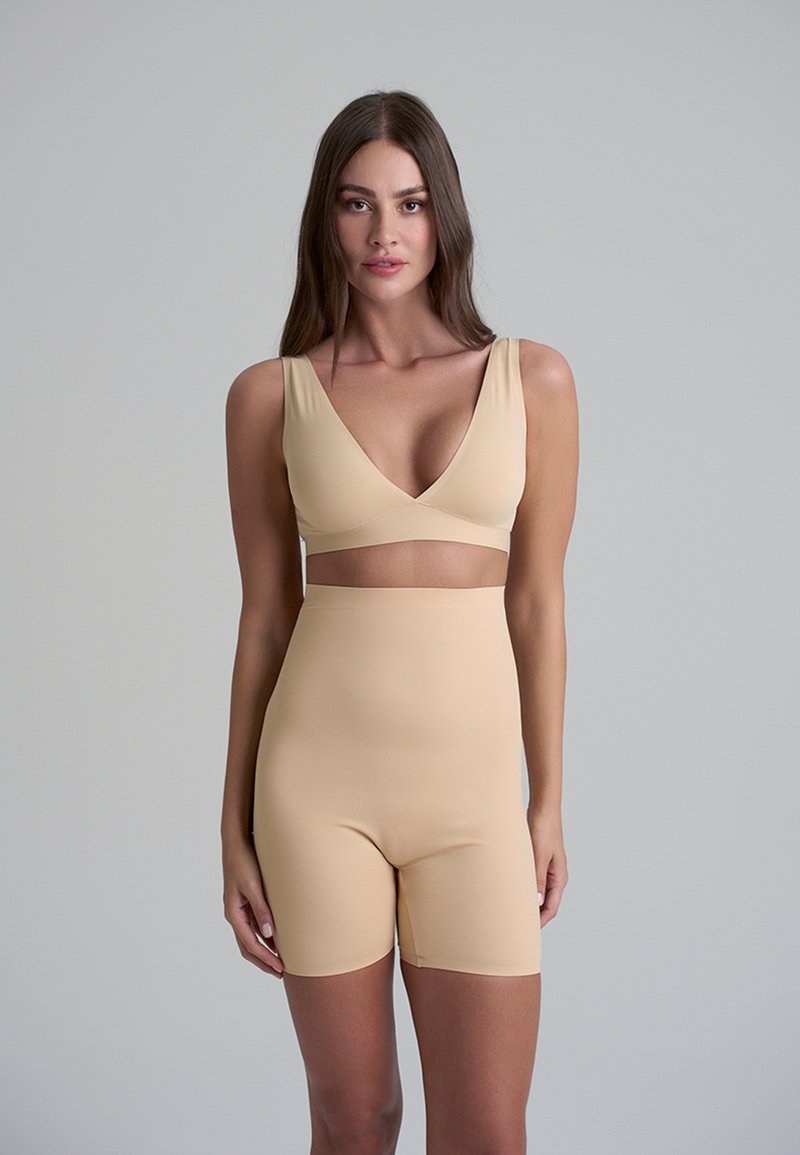 Set di shapewear beige che presenta un reggiseno a V e shorts a vita alta. Realizzato in un materiale liscio e elasticizzato con dettagli delle cuciture minimi.