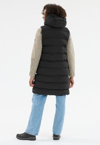 Svart puffärmad väst med kviltad design, huva och grå långärmad tröja. Bärs med ljusblå jeans och svarta skor.