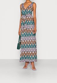 Robe maxi avec un motif en zigzag turquoise, rose et orange. Fabriquée en tissu léger, avec une taille cintrée et un décolleté en V profond.