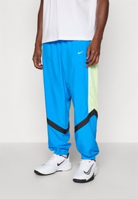 Light blue athletic pants with black accents and lime green mesh detail on the side. Elastic cuffs and a slim fit. Nike logo displayed.