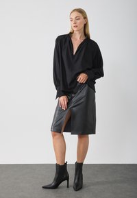 Svart bluse med dyp V-hals og voluminøse ermer, kombinert med et tettsittende svart skinnskjørt med en frontsplitt. Sorte ankelstøvler fullfører looken.