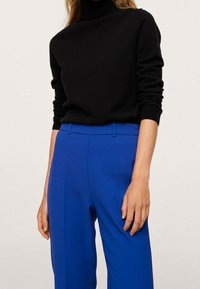 Pull noir à col roulé en matière douce associé à un pantalon taille haute à jambes droites de couleur bleu vif, mettant en valeur une texture lisse.