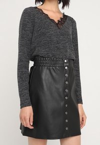 Haut à manches longues en maille grise avec bordure en dentelle noire, associé à une jupe taille haute en similicuir noir avec fermetures à boutons-pression.