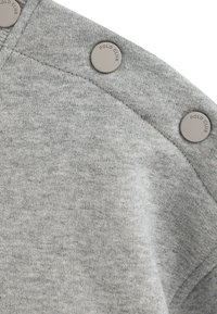 Tessuto di felpa grigia con una consistenza morbida, caratterizzato da quattro bottoni a pressione grigi in plastica con la dicitura "POLO CLUB" sulla spalla.