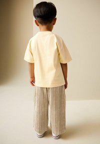 Hellgelbes Baumwoll-T-Shirt und beige gestreifte, weit geschnittene Hosen. Das Outfit besticht durch weiche Texturen und eine lockere Passform, kombiniert mit weißen Schuhen.