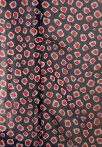 Tissu sombre présentant un motif dispersé de formes irrégulières rouges et blanches, avec une texture subtile et une finition lisse.