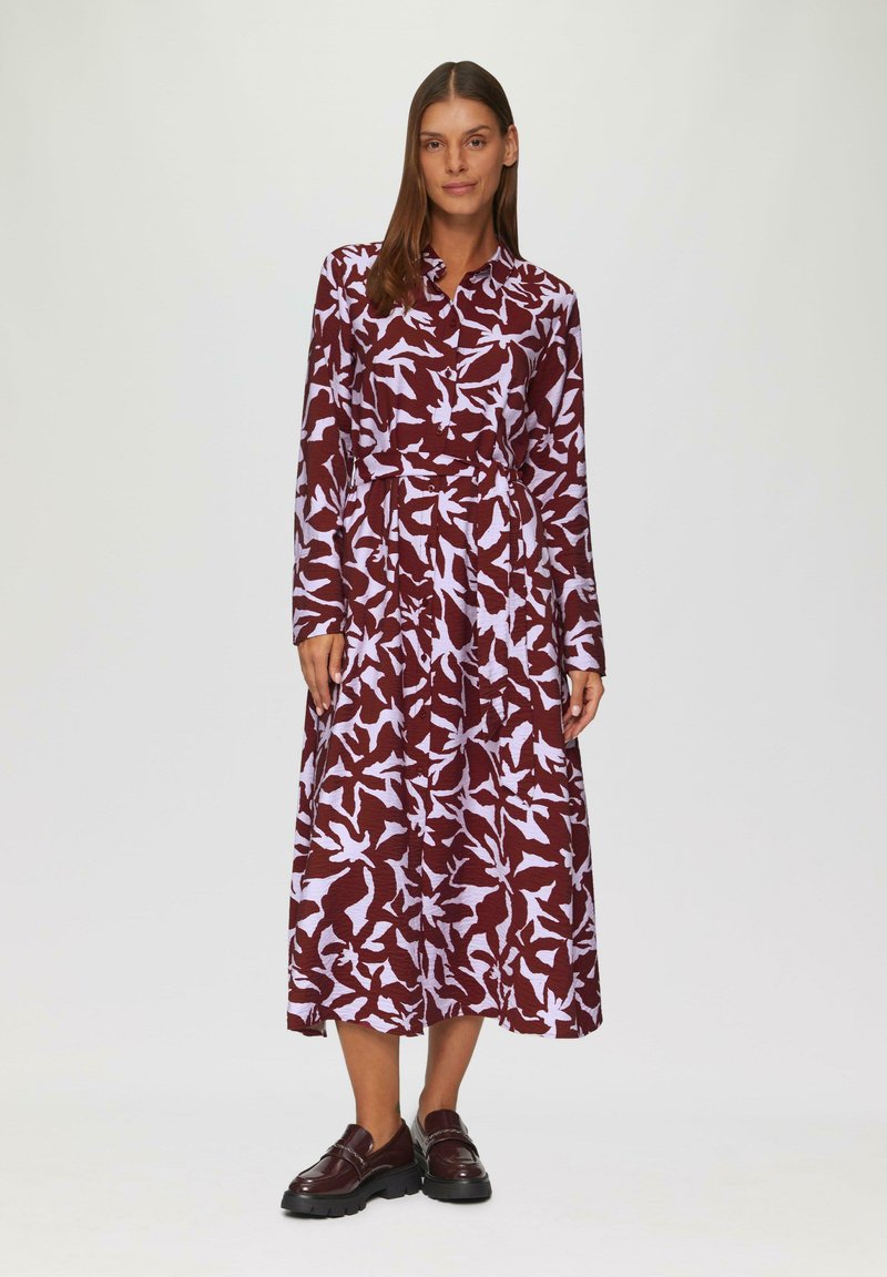 Długa, bordowa sukienka z białym, abstrakcyjnym wzorem liści. Posiada zapięcie na guziki przy kołnierzyku, długie rękawy oraz dopasowaną talie. Materiał o fakturze.