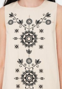 Vestido sin mangas beige con delicados bordados negros que presentan patrones florales y geométricos, acentuados con detalles en azul claro y rosa.