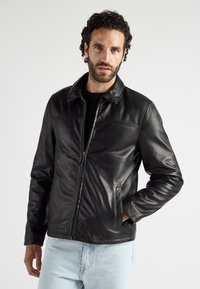 Zwarte leren jas met een kraag, gladde textuur, voorzakken en een ritssluiting, gecombineerd met lichtblauwe denim jeans.