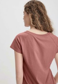 Camiseta de manga corta rosa con cuello redondo, confeccionada en tejido suave, que presenta un corte relajado y una textura lisa.