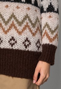 Knitted sweater with a light cream, brown, and olive color palette. Features geometric patterns and a ribbed dark brown hem and cuffs.