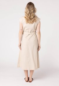 Beżowa lniana sukienka z rękawami typu cap, z paskiem w talii i luźną spódnicą sięgającą do połowy łydki. Gładka faktura, minimalistyczny design.