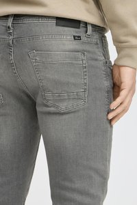 Jeans de mezclilla gris de corte ajustado, con dos bolsillos traseros, costuras sutiles y una etiqueta de cuero negro en la cintura.