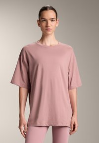 Oversized short-sleeve t-shirt in soft dusty pink fabric, featuring a rounded neckline and relaxed fit. Smooth texture, minimalistic design.