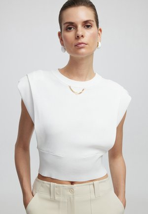 T-shirt blanc court avec des manches courtes, en tissu lisse. Présente un col rond et des détails de couture subtils.