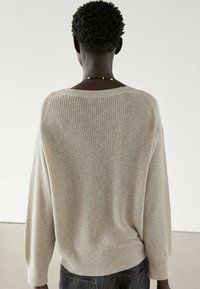 Pull en tricot beige à coupe ample, avec des manches raglan et un ourlet côtelé. La texture est douce, avec un motif subtil créé par le tricot.