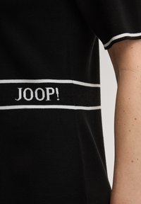 Μαύρο ύφασμα με λευκές ρίγες που φέρει το κείμενο "JOOP!" πλεκτό στο σχέδιο. Το ένδυμα έχει ομαλή υφή και κοντά μανίκια.