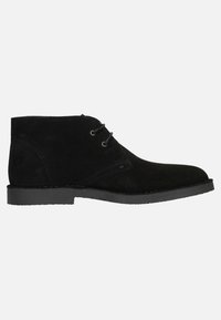 Bottine chukka en daim noir avec deux œillets, semelle plate en caoutchouc noir, détails piqués et bout rond. La surface paraît lisse et texturée.