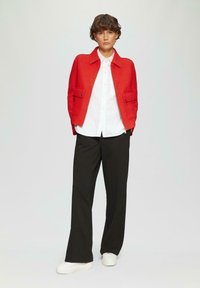 Czerwona wełniana kurtka z kołnierzem, dwoma przednimi kieszeniami i guzikami jako ozdobą. Pod kurtką biała koszula, zestawiona z czarnymi spodniami o szerokich nogawkach i białymi sneakersami.