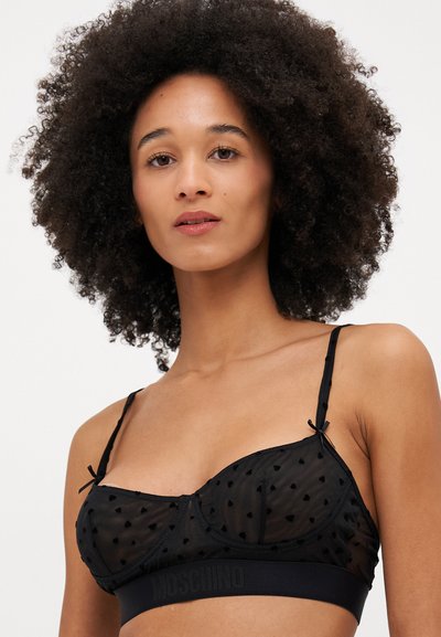 Sostenes de malla negra con patrones en forma de corazón, tirantes ajustables y una banda elástica con marca. Textura suave con un diseño transparente.