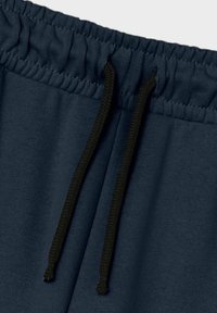 Pantaloni della tuta blu navy con cintura elastica e lacci neri annodati davanti.