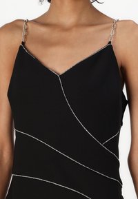 Svart klänning med V-ringning och silverkedjespännen. Har diagonala silverdetaljer över tyget, vilket skapar en texturerad kontrast.