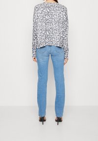 Kevyt harmaa paita, jossa leopardikuvio, löysä istuvuus ja pitkät hihat, yhdistettynä istuviin vaaleansinisiin farkkuihin ja mustiin korkokenkiin.