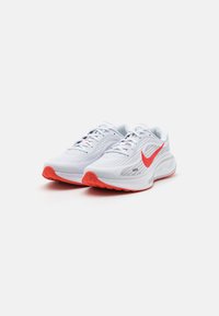 Hvite treningssko med mesh-overdel, med en fremtredende rød swoosh og en teksturert rød yttersåle. Designet for komfort og ytelse.