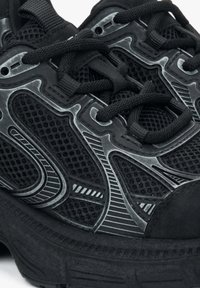 Czarny but sportowy z siateczkową cholewką i odblaskowymi szarymi akcentami, teksturowanymi sznurowadłami oraz grubą gumową podeszwą.