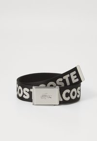 Ceinture tissée noire avec le texte "LACOSTE" en blanc, boucle en métal avec logo crocodile embossé et texture lisse.