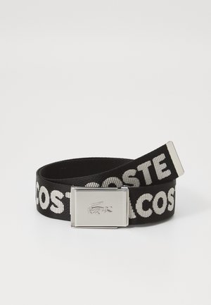 Black woven belt featuring white "LACOSTE" text, metal buckle with embossed crocodile logo, and a smooth texture.