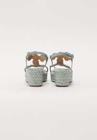 Deux sandales vues de dos, présentant une tige en suede bleu clair avec des semelles en jute tressé et des motifs décoratifs découpés.