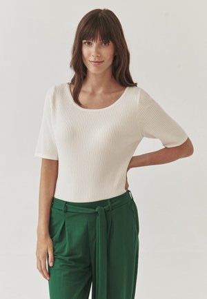 Top bianco a coste con maniche corte, caratterizzato da un collo rotondo, abbinato a pantaloni verdi a vita alta con cintura annodata. La texture è liscia.